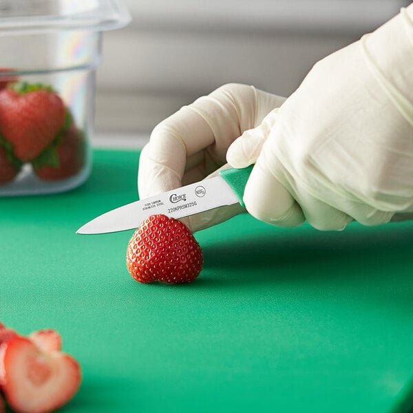 A person holding a Choice paring knife with a green handle cutting a strawberry.