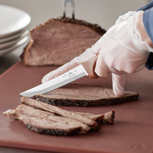 A person using a Choice 6" serrated utility knife to cut meat.
