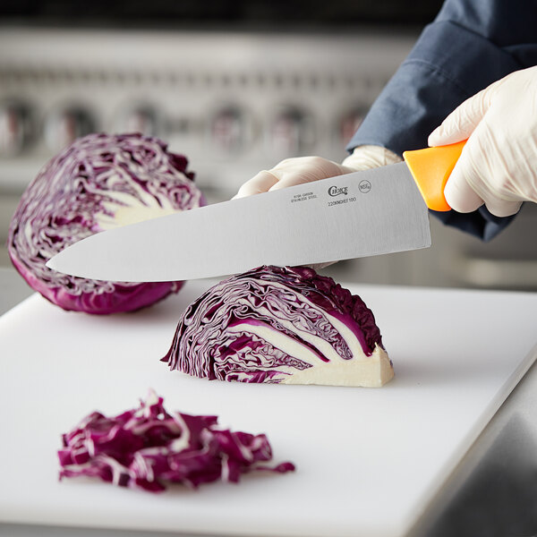 A person using a Choice 10" chef knife to cut cabbage on a cutting board.