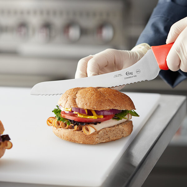 A person in gloves using a Choice bread knife to cut a sandwich.