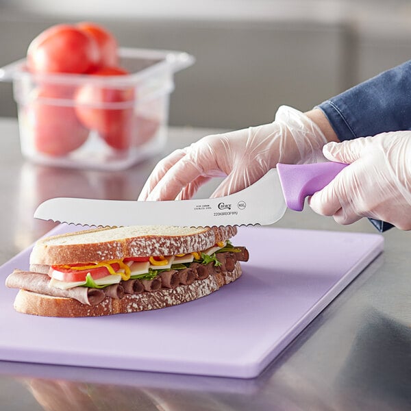 A person cutting a sandwich with a Choice bread knife on a purple cutting board.