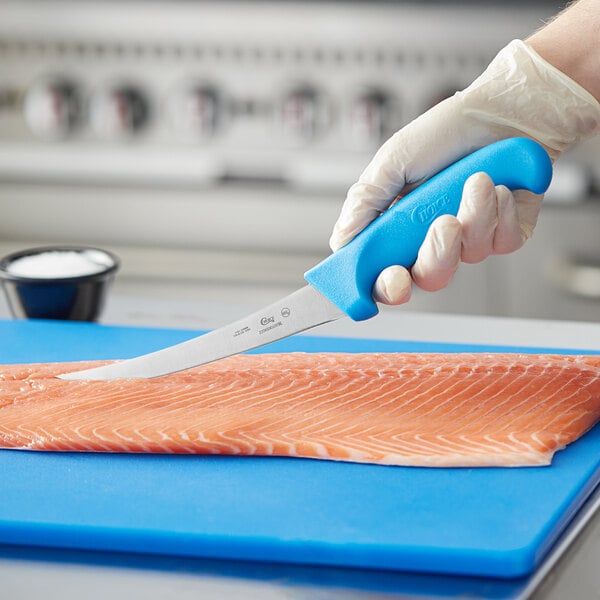 A hand holding a Choice curved boning knife with a blue handle cutting a piece of salmon.