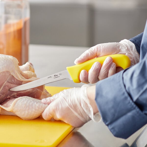 A person using a Choice narrow stiff boning knife with a yellow handle to cut a chicken.