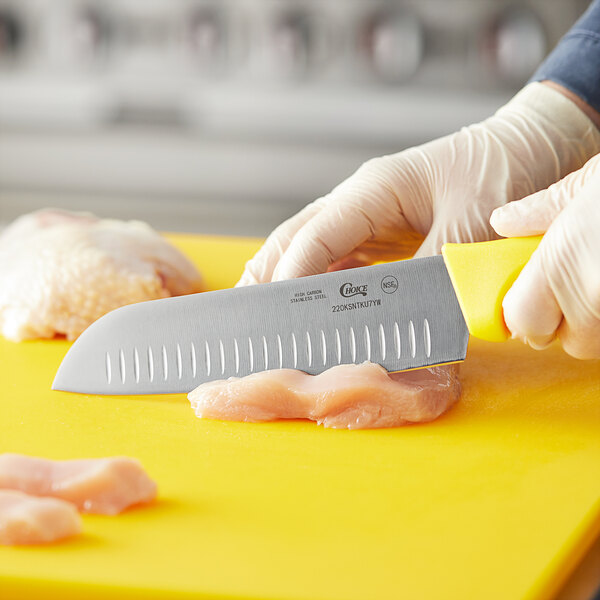 A person in gloves cutting meat with a Choice 7" Santoku Knife on a cutting board.