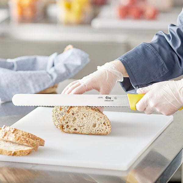 A person cutting bread with a Choice yellow serrated bread knife.