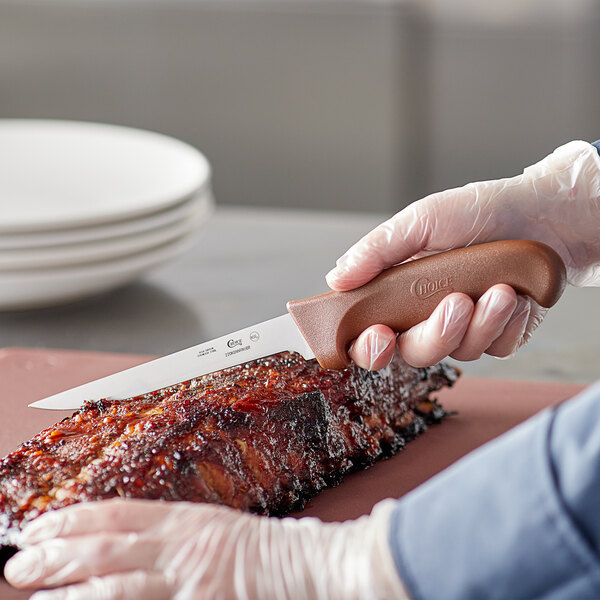 A person using a Choice 6" Narrow Stiff Boning Knife to cut meat.