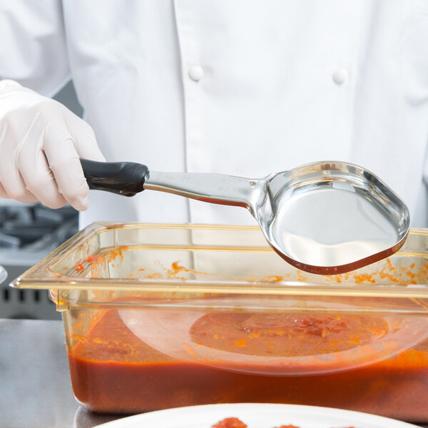 A person in white gloves using a Vollrath Black Solid Oval Spoodle to serve food.