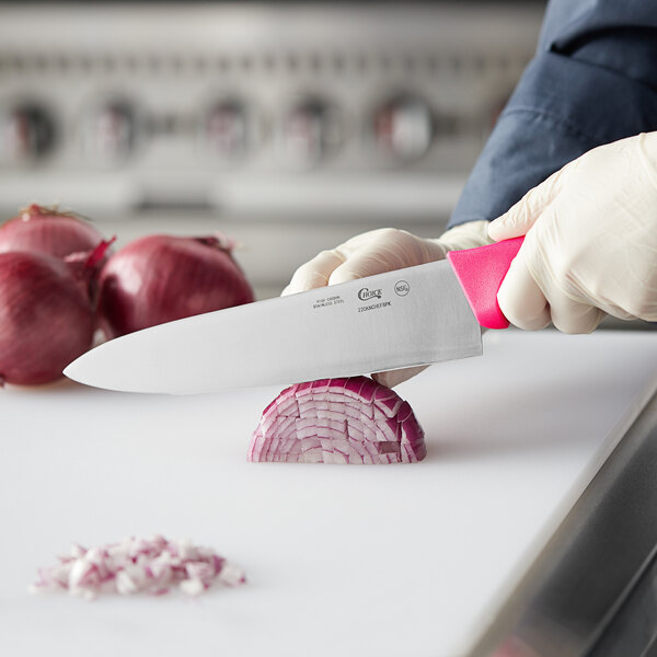 A person using a Choice 8" Chef Knife with a neon pink handle to cut a red onion on a counter.