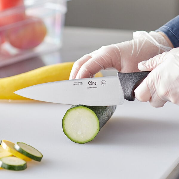 A person using a Choice 6" Chef Knife to cut a zucchini.
