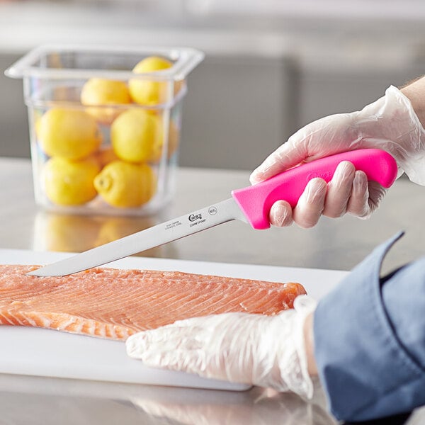 A person holding a Choice neon pink fillet knife cutting a piece of salmon.