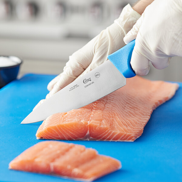 A person in gloves using a Choice chef knife to cut a piece of salmon on a blue cutting board.