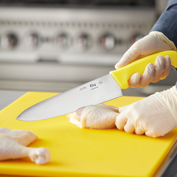 A person in gloves using a Choice 8" chef knife to cut chicken on a yellow cutting board.