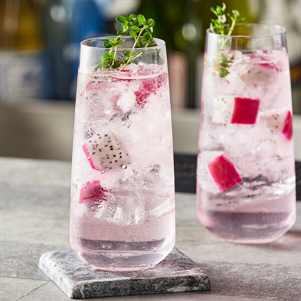 Two Nude Mirage highball glasses filled with pink drinks, ice, and a sprig of thyme.