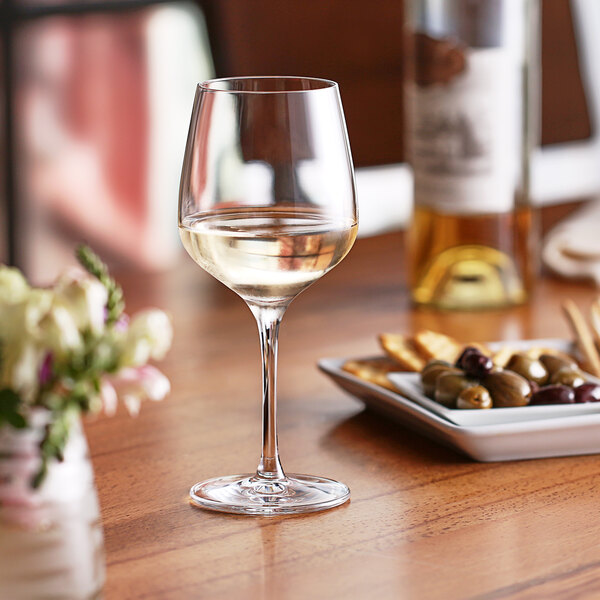 A Nude Refine white wine glass filled with white wine on a table.