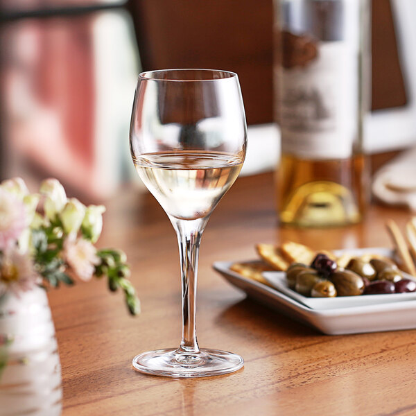 A Nude Primeur wine goblet filled with white wine on a table.