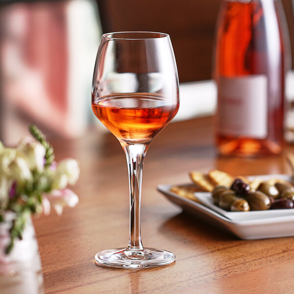 A Nude Fame wine glass filled with pink liquid sits on a table.
