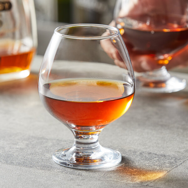 A Pasabahce brandy glass being filled with brown liquid.