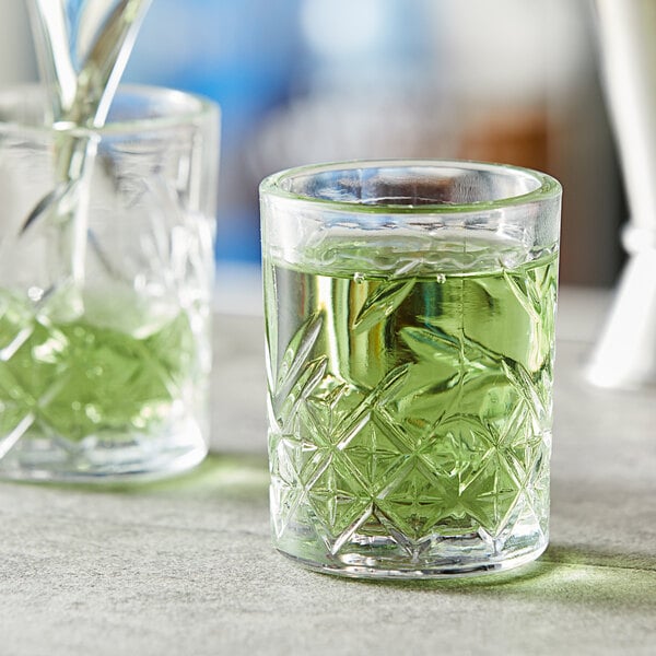Two Pasabahce Timeless Vintage shot glasses filled with green liquid on a table.