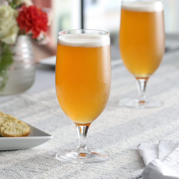 Two Nude Primeur stemmed beer glasses filled with beer on a table in a brewery tasting room.