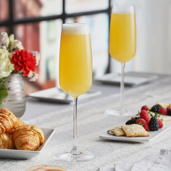 A table with pastries, orange juice, and Nude Mirage flute glasses filled with yellow liquid.