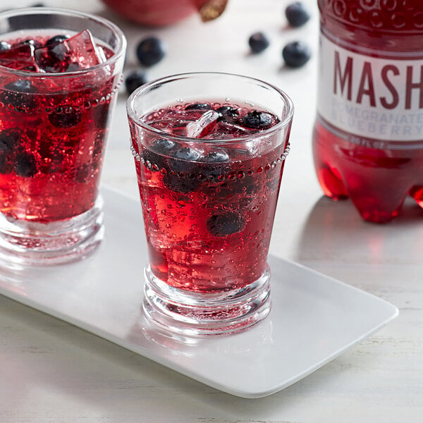 Two glasses of Boylan Mash Pomegranate Blueberry juice with ice and berries on a white plate.