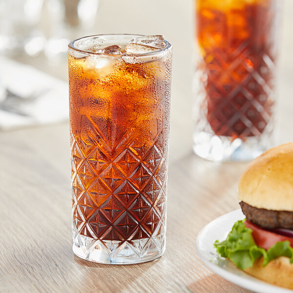 A Pasabahce Timeless Vintage long drink glass filled with iced tea on a table with a hamburger.