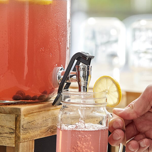 A person using an Acopa silver spigot to pour pink lemonade into a glass jar.