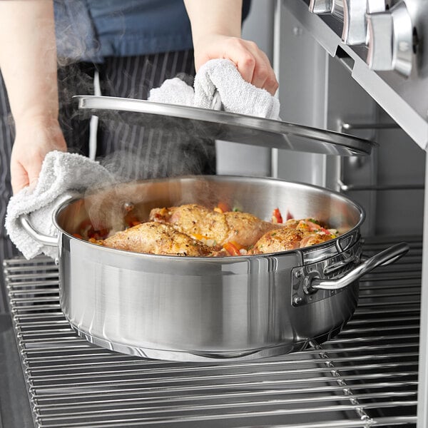 A person using a Vigor stainless steel brazier to cook chicken.