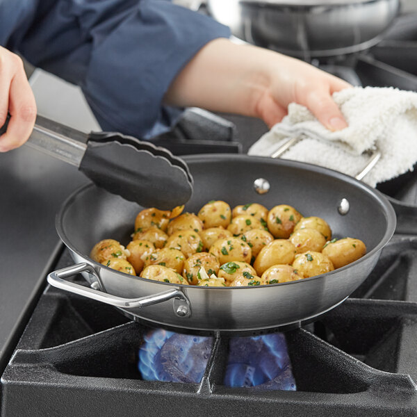 A person using a Vigor stainless steel non-stick fry pan to cook potatoes on a stove.