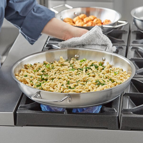 A person cooking pasta in a Vigor stainless steel fry pan on a stove.