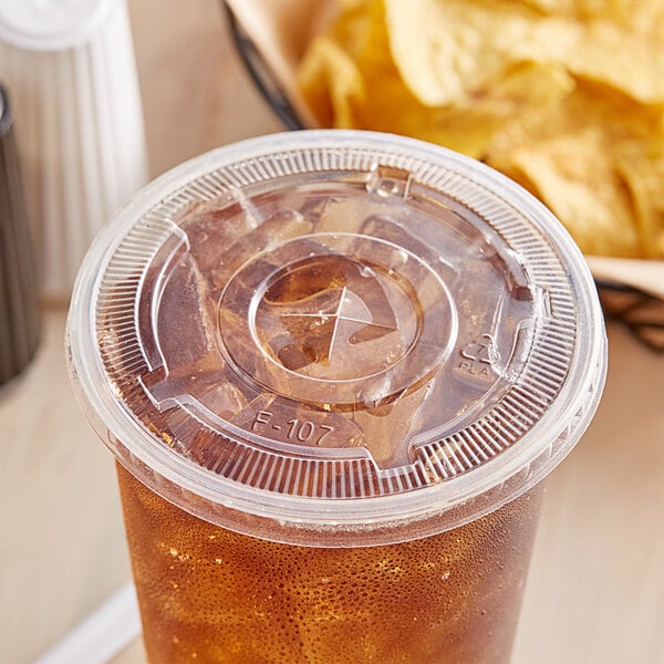 A clear EcoChoice plastic cup lid with a straw slot on a plastic cup with a drink in it.