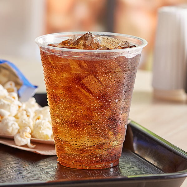 A EcoChoice compostable plastic cup filled with ice tea on a plate of popcorn.