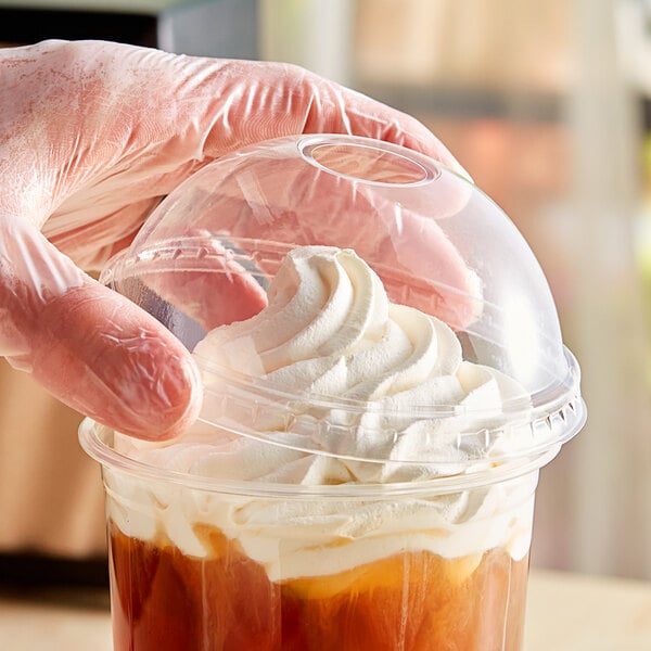 A hand holding a plastic container of whipped cream with a PLA compostable plastic dome lid with a hole.