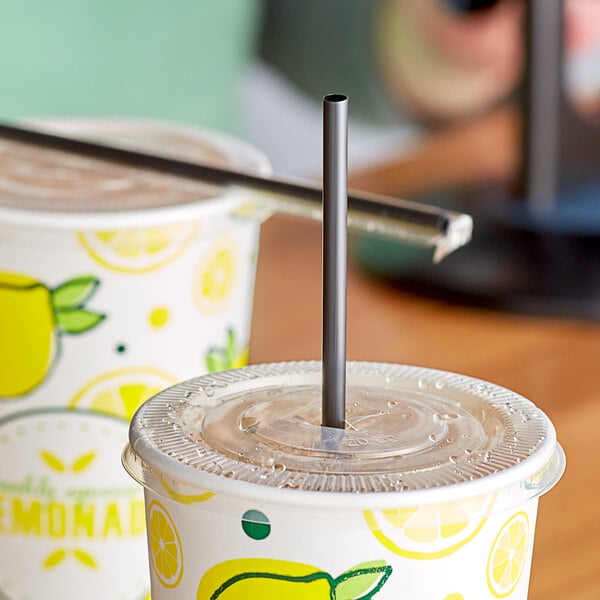 Two cups of lemonade with Choice jumbo black straws on a table.
