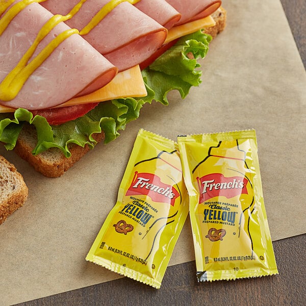 A sandwich with ham, cheese, and French's Classic Yellow Mustard on a table in a deli.