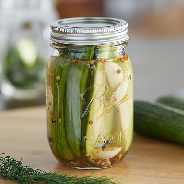 A Ball pint jar of pickles with dill and spices on a table.