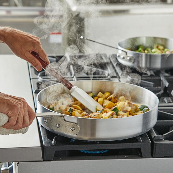 A person cooking food in a Choice aluminum saute pan on a stove.