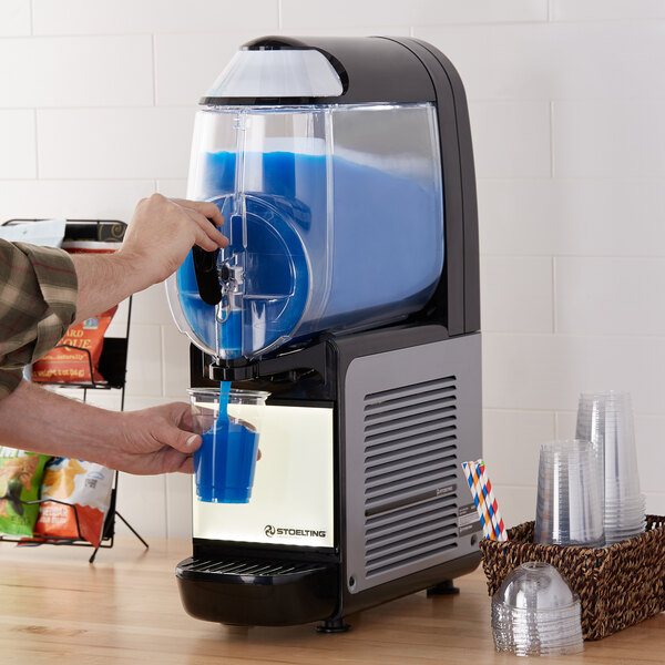 A person pouring blue liquid into a Stoelting frozen beverage machine.