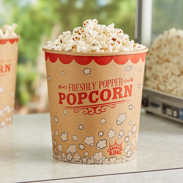 A close up of a Carnival King 130 oz. popcorn bucket on a table with two boxes of popcorn with red text.