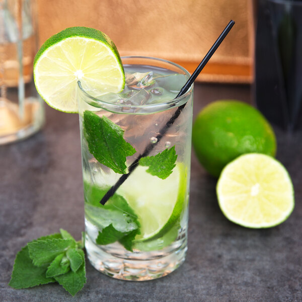 A Libbey highball glass filled with water, ice, limes, and mint with a straw and lime wedge.