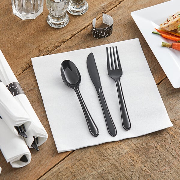 A white napkin with a black fork, spoon, and knife on it.
