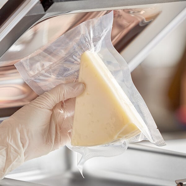 A gloved hand holds a piece of cheese in a Choice vacuum packaging pouch.