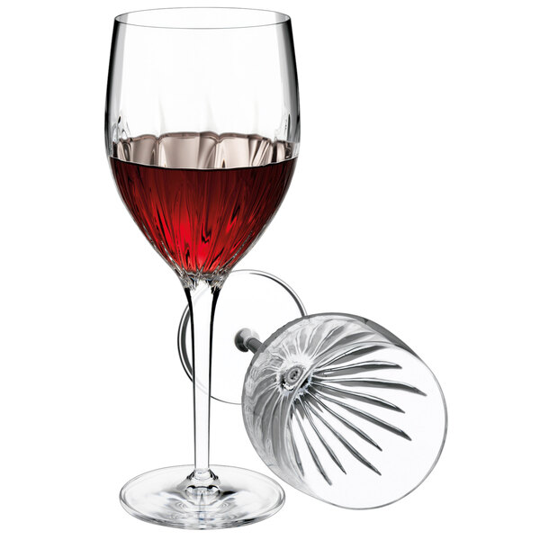 A Luigi Bormioli red wine glass filled with red wine on a table in a winery cellar.
