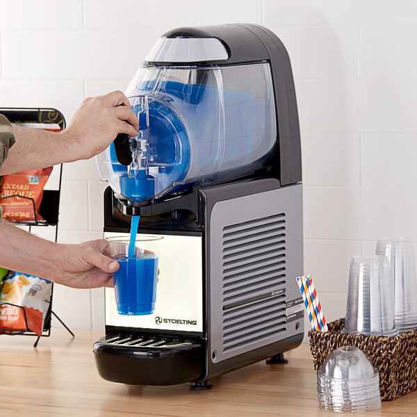 A person pouring blue liquid from a Stoelting frozen beverage machine into a glass.