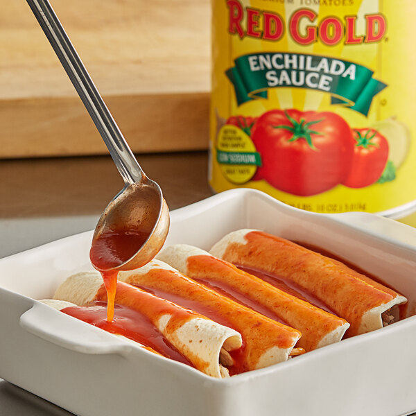 A spoon pouring Red Gold enchilada sauce onto enchiladas on a white plate.