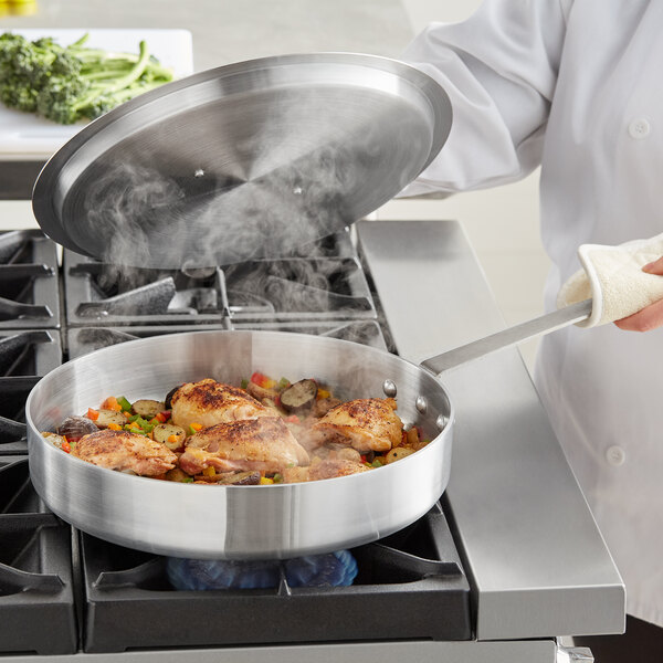 A chef using a Choice aluminum saute pan to cook food on a stove.
