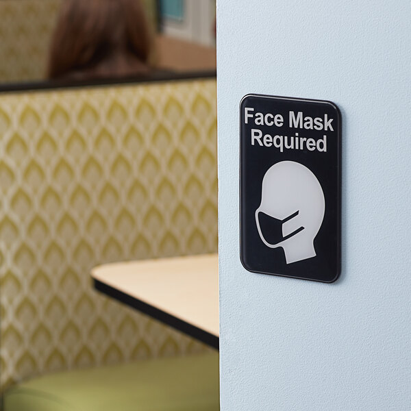 A Tablecraft plastic sign on a wall that says "Face Mask Required" in black and white.