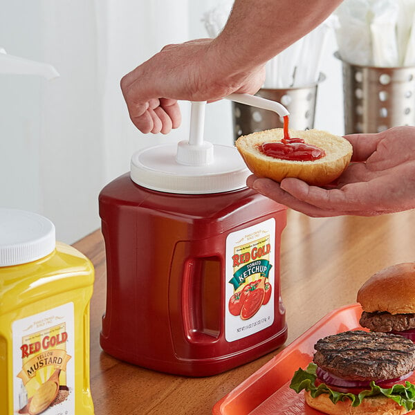 A person using a pump to add Red Gold Ketchup to a hamburger bun.