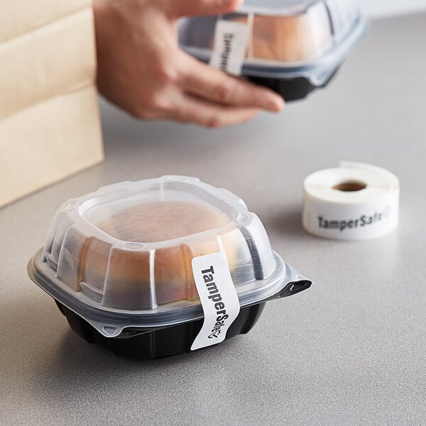 A hand using a TamperSafe white paper label to seal a plastic container of food.