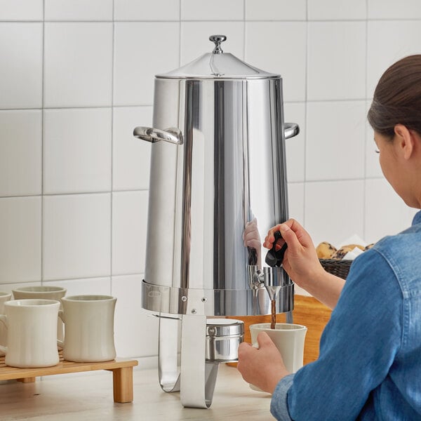 A woman using a Choice Economy Stainless Steel coffee chafer urn to pour coffee into a white mug.